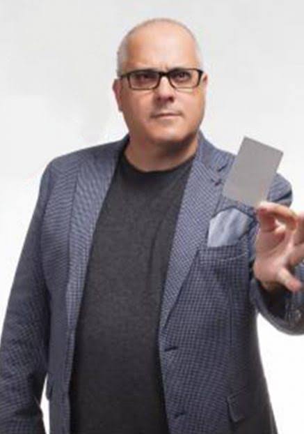 Miguel Puga, MagoMigue, con americana azul, muestra una carta en la mano